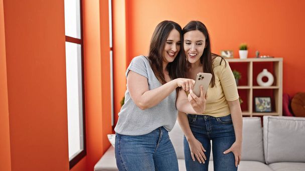 Two women smiling confident using smartphone at home - 写真・画像