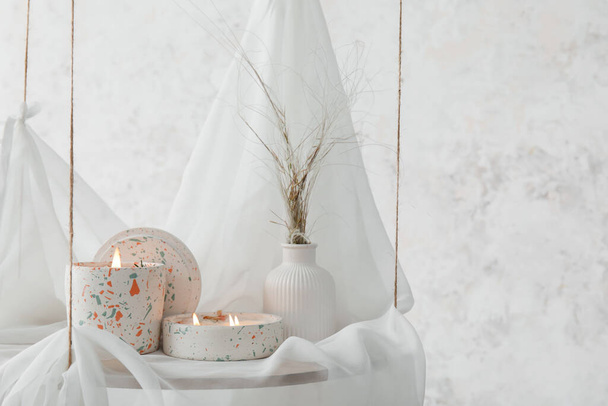 Holders with burning candles on hanging shelf near light wall in room, closeup - Foto, Bild