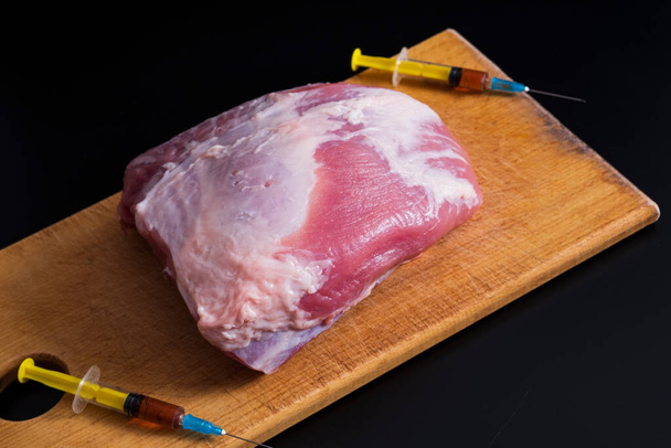 Injection from a syringe into raw meat on a dark background.Conceptual illustration of hormones and antibiotics in food production. - Photo, Image