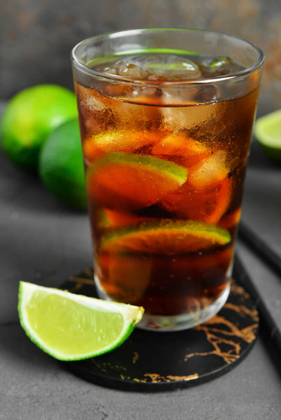Glass of cold Cuba Libre cocktail and limes on grey table - Фото, изображение