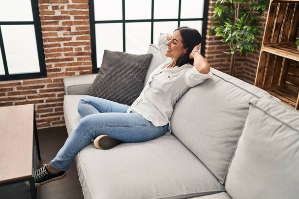 Young beautiful hispanic woman relaxed with hands on head sitting on sofa at home - Fotoğraf, Görsel
