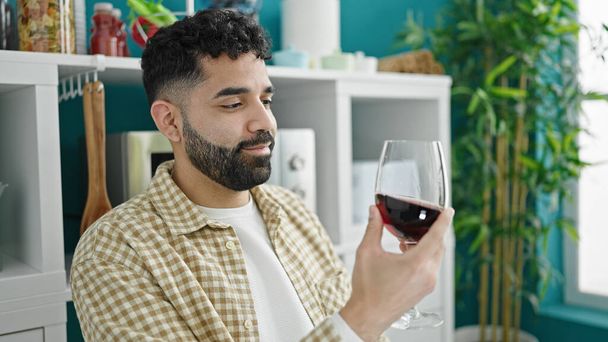 Young hispanic man drinking glass of wine sitting on table at dinning room - Fotoğraf, Görsel