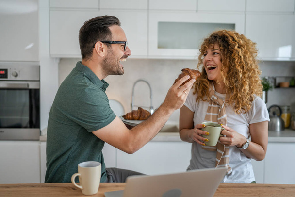 Kaukaska para mężczyzna i kobieta jedzący śniadanie w kuchni jedzą rogaliki i kawę codziennie rano rutynowe domowe życie rodzinne prawdziwi ludzie kopiują przestrzeń - Zdjęcie, obraz