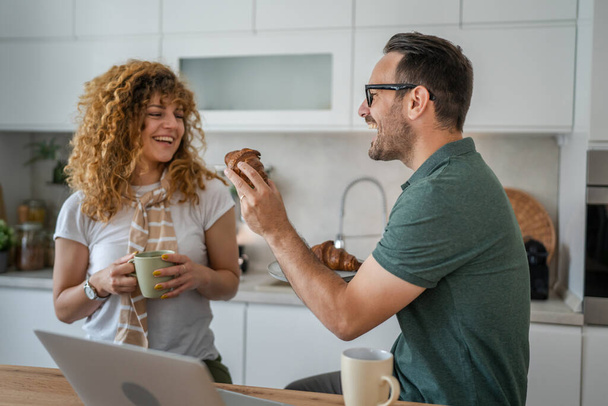 Valkoihoinen pari mies ja nainen, joilla on aamiainen keittiössä, syövät croissantia ja kahvia päivittäin aamulla rutiini kotielämä oikeat ihmiset kopioivat tilaa. - Valokuva, kuva