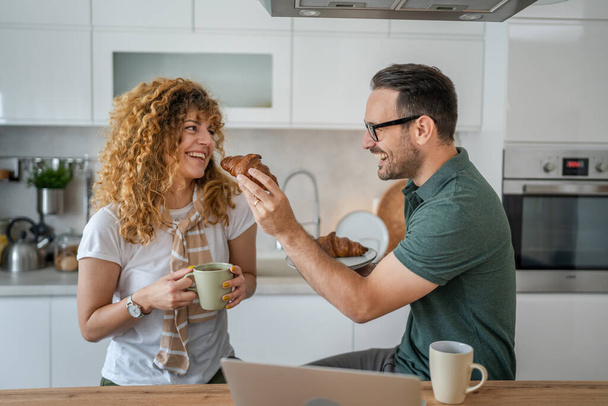 Caucásico pareja hombre y mujer desayunando en la cocina comer croissant y café todos los días por la mañana rutina doméstica vida familiar personas reales copiar espacio - Foto, Imagen