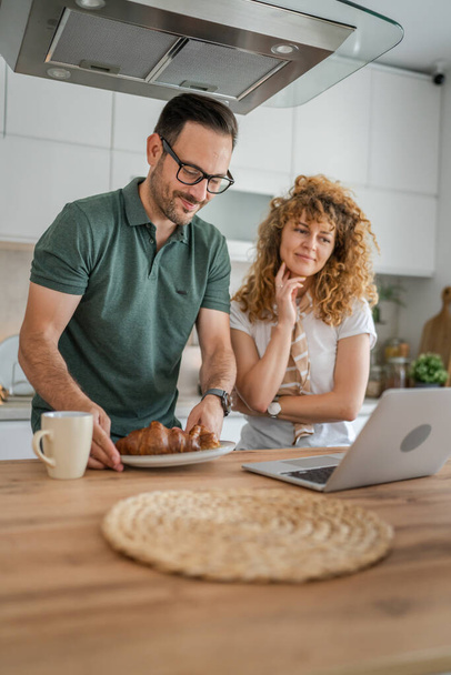 Caucasian couple man and woman having breakfast in the kitchen eat croissant and coffee daily morning routine domestic family life real people copy space - 写真・画像