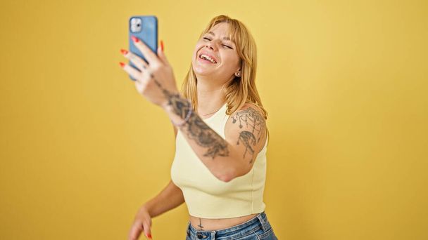 Молода блондинка посміхається впевнений, що має відеодзвінок над ізольованим жовтим тлом - Фото, зображення