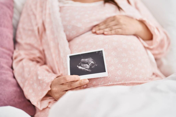 Giovane donna incinta toccare pancia tenendo ecografia in camera da letto - Foto, immagini