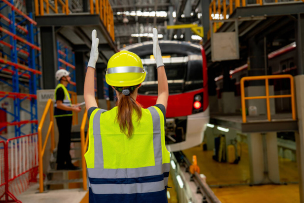 A technikus vagy a gyárban dolgozó nő áll, és bemutatja az akciót a járművezetőnek az elektromos vonaton a gyárban és a munkatárs is marad a vonat közelében. - Fotó, kép