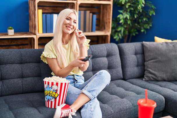 Mujer rubia joven viendo la película sentada en el sofá en casa - Foto, imagen