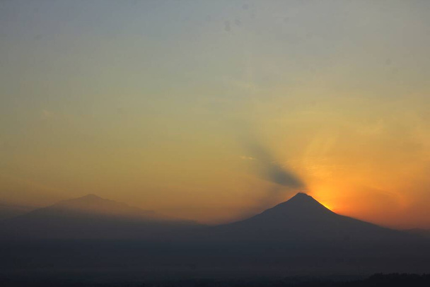 Силует гори Мерапі з червонувато-помаранчевим небом на світанку. Вулкан з вулканом типу Stratovolcano розташований в районах Джок'якарта і Центральна Ява.. - Фото, зображення