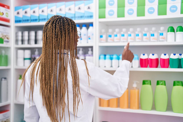 Africano americano farmacêutico mulher segurando desodorante de estantes na farmácia - Foto, Imagem