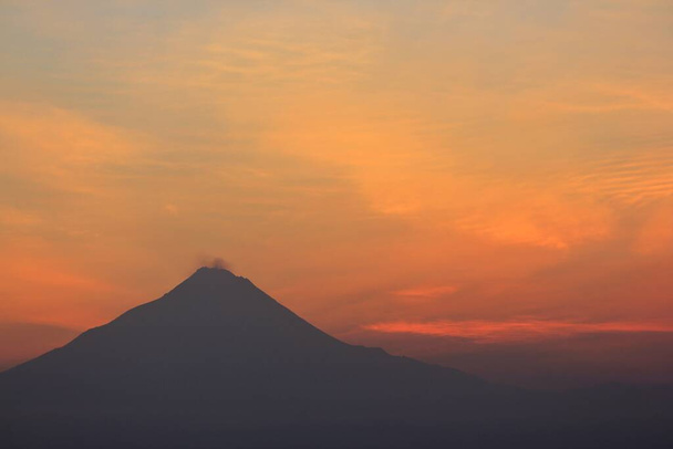Silueta del Monte Merapi con un cielo rojo anaranjado al amanecer. Este volcán con un tipo de erupción Stratovolcán se encuentra en las regiones de Yogyakarta y Java Central. - Foto, imagen