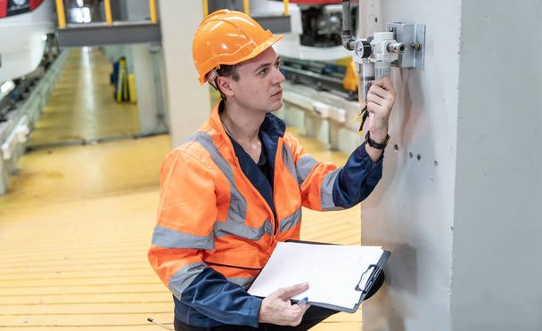 uomo bianco in uniforme e casco ispeziona i sistemi elettrici in una fabbrica di treni elettrici. - Foto, immagini