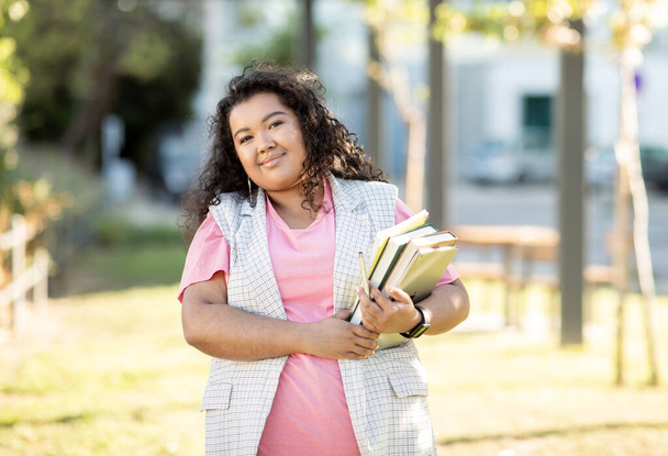 Portrait Of Plus Size Student Woman Holding Workbooks And Digital Tablet Smiling To Camera Standing Outdoors After Classes. Learner Lady Posing With Her Books At College Campus Park - Fotoğraf, Görsel