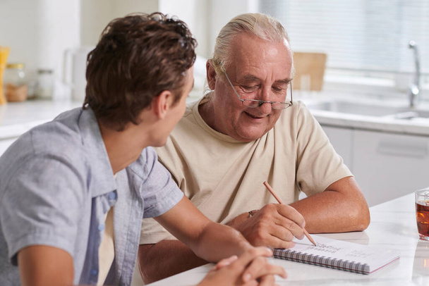 Улыбающийся пожилой человек объясняет внуку, как планировать бюджет - Фото, изображение