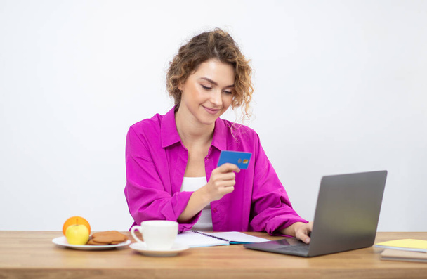 Płatności online. Uśmiechnięta młoda kobieta korzystająca z laptopa i karty kredytowej, siedząca przy biurku w biurze, szczęśliwa Millenium Freelancer Lady kupująca z Internetu, korzystająca z e-commerce, przestrzeń kopiująca - Zdjęcie, obraz