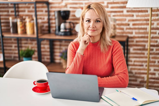 Jeune femme blonde souriant confiant en utilisant un ordinateur portable à la maison - Photo, image