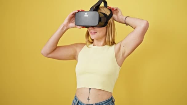 Giovane donna bionda che gioca al videogioco utilizzando occhiali di realtà virtuale su sfondo giallo isolato - Filmati, video