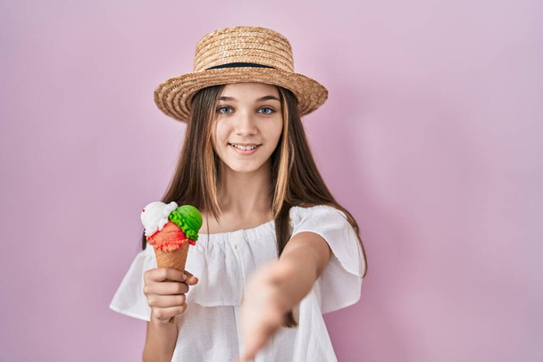 Chica adolescente sosteniendo helado sonriente amistoso ofreciendo apretón de manos como saludo y bienvenida. negocios exitosos.  - Foto, Imagen