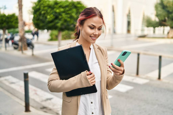 Молода кавказька жінка бізнесмен, використовуючи смартфон тримає зв'язуючу на вулиці
 - Фото, зображення