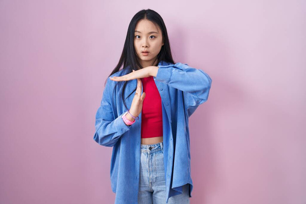 Young asian woman standing over pink background doing time out gesture with hands, frustrated and serious face  - Photo, Image