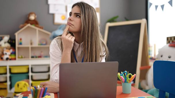Jovem bela mulher hispânica professora pré-escolar usando laptop pensando no jardim de infância - Foto, Imagem