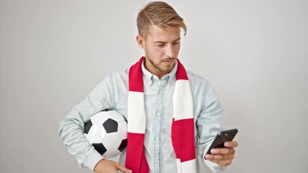 Joven hombre caucásico apoyando equipo de fútbol usando teléfono inteligente sobre fondo blanco aislado - Metraje, vídeo