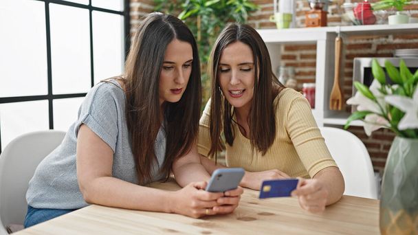 Zwei Frauen kaufen online mit Smartphone und Kreditkarte im Esszimmer ein - Foto, Bild