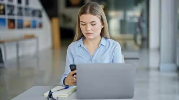 Mujer joven rubia trabajadora de negocios usando smartphone con gesto ganador en la oficina - Imágenes, Vídeo