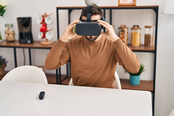 Young hispanic man playing video game using virtual reality glasses at home - Foto, Imagen