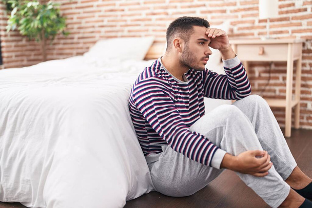 Joven hispano estresado sentado en el suelo en el dormitorio - Foto, Imagen