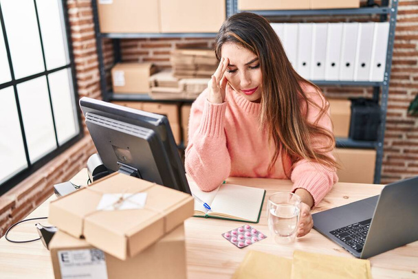 Jonge mooie Spaanse vrouw e-commerce zakenman het nemen van pillen op kantoor - Foto, afbeelding