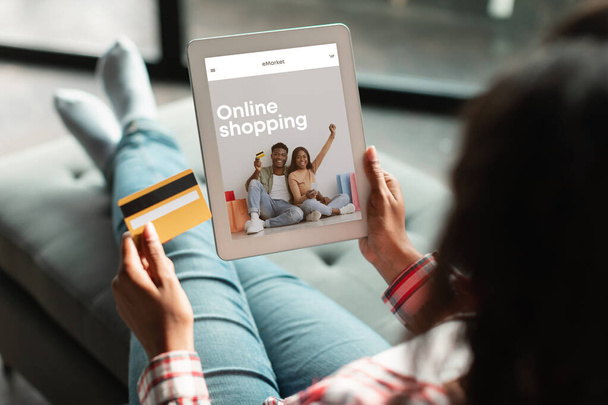 Ekranında moda mağazası ve kredi kartı olan dijital tablet kullanan genç siyahi bir kadın sipariş ve hizmetleri internetten ödüyor. Müşteri kıyafetlerini uygulamadan, web sitesinden alır - Fotoğraf, Görsel