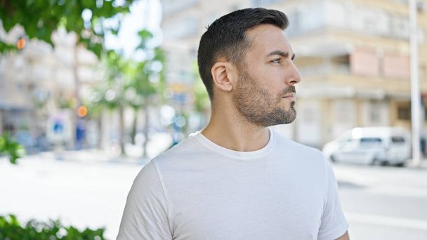 Молодий іспаномовний чоловік дивиться в бік з серйозним виразом на вулиці
 - Фото, зображення