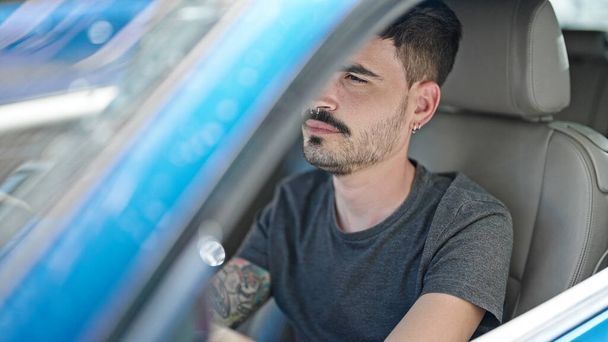 Junger hispanischer Mann fährt Auto mit entspanntem Gesichtsausdruck auf der Straße - Foto, Bild