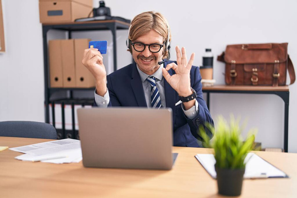 Caucasian man with mustache working at the office doing online shopping doing ok sign with fingers, smiling friendly gesturing excellent symbol  - Photo, Image