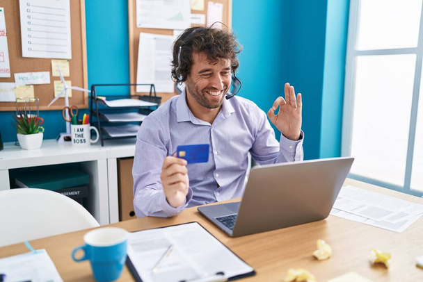 Spaanse jongeman werkt op kantoor doet online winkelen doen ok teken met de vingers, glimlachend vriendelijk gebaar uitstekende symbool  - Foto, afbeelding