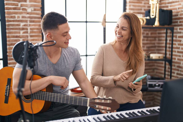 Чоловік і жінка музиканти мають класичний гітарний урок, використовуючи смартфон в музичній студії
 - Фото, зображення