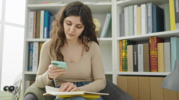 Молода красива студентка-іспанка використовує книгу для читання смартфонів в бібліотечному університеті - Фото, зображення