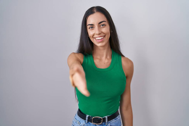 Young woman standing over isolated background smiling friendly offering handshake as greeting and welcoming. successful business.  - Foto, immagini