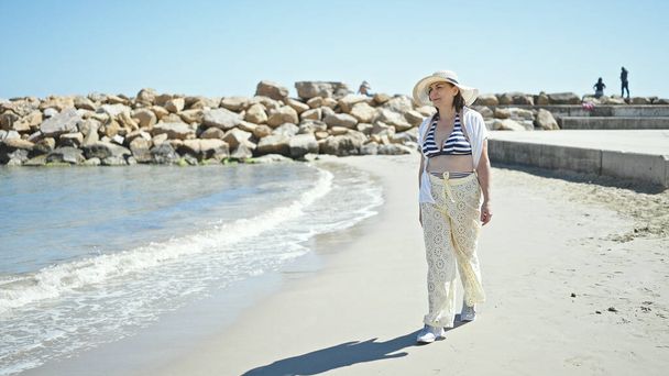 Middelbare leeftijd Spaanse vrouw toerist draagt bikini op het strand - Foto, afbeelding