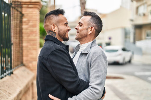 Двое мужчин улыбаются уверенно обнимая друг друга на улице - Фото, изображение