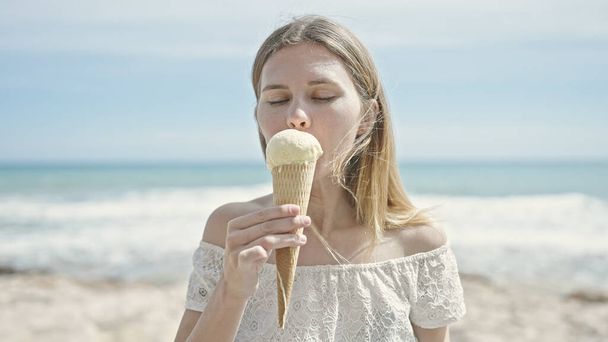 Kumsalda dondurma yiyen genç sarışın kadın. - Fotoğraf, Görsel
