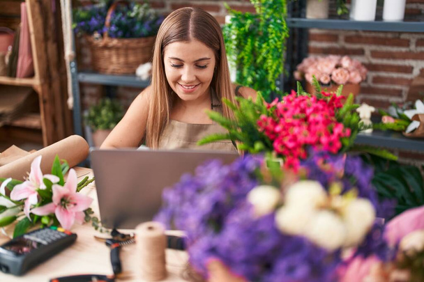 Jovem bela florista mulher hispânica sorrindo confiante usando laptop na florista - Foto, Imagem