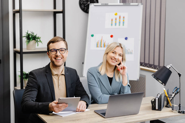 Start up business team on meeting in modern office interior, working on laptop and tablet. A young woman and a man are sitting at the table and working on a business project. - Valokuva, kuva