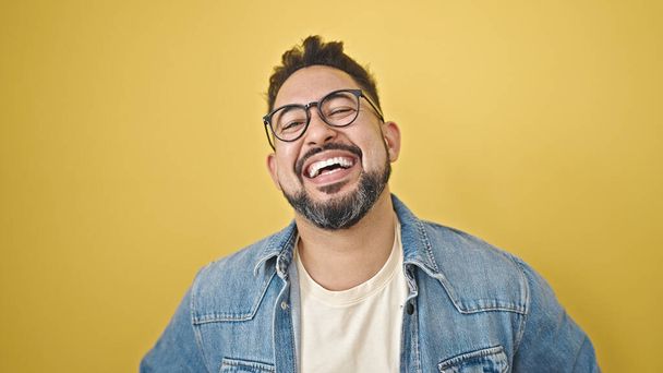 Junger lateinischer Mann lächelt selbstbewusst vor isoliertem gelben Hintergrund - Foto, Bild