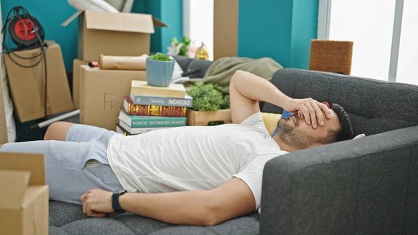 Nuori latino mies makaa sohvalla stressaantunut uudessa kodissa - Valokuva, kuva