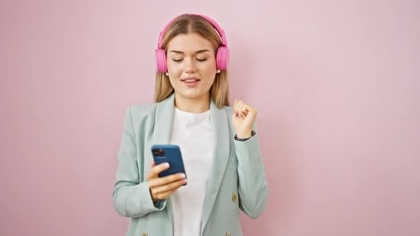 Młoda blondynka biznes pracownik słuchanie muzyki i taniec na odizolowanym różowym tle - Materiał filmowy, wideo