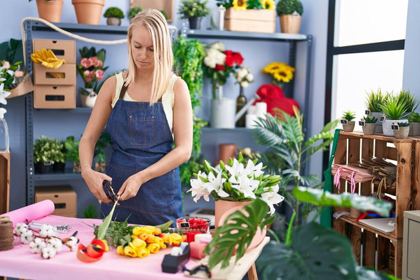 Молодая блондинка флорист стрижет стебель в цветочном магазине - Фото, изображение